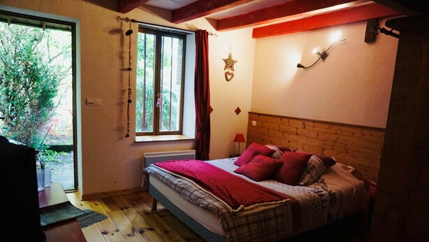 Een slaapkamer met een houten hoofdbord, een bed met rode en gestreepte beddengoed, een raam met gordijnen, en een sterren decoratie aan de muur.