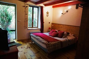 Une chambre avec une tête de lit en bois, un lit avec une literie rouge et à motifs, une fenêtre avec des rideaux et une décoration en forme d’étoile sur le mur.