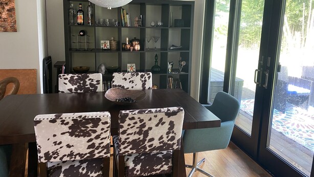 A dining area with a dark wooden table and chairs with a cowhide pattern. A decorative bowl is on the table. Behind the table is a dark green bookshelf filled with various items. - Cute, cozy rancher close to down town Annapolis (Annapolis)
