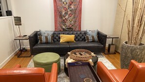 A living room with a black sofa, orange chairs, a small table, and a patterned rug. - Cute, cozy rancher close to down town Annapolis (Annapolis)