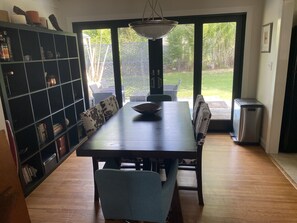 A dining area with a large table, chairs, a bookshelf, and a view through large windows. - Cute, cozy rancher close to down town Annapolis (Annapolis)
