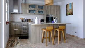 A modern kitchen with wooden cabinets, a central island with bar stools, a hanging light fixture, and a painting on the wall.