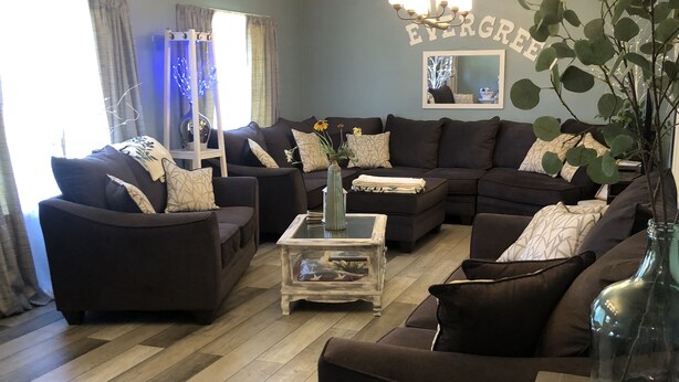 Een woonkamer met donkere banken, een glazen salontafel en een kroonluchter.