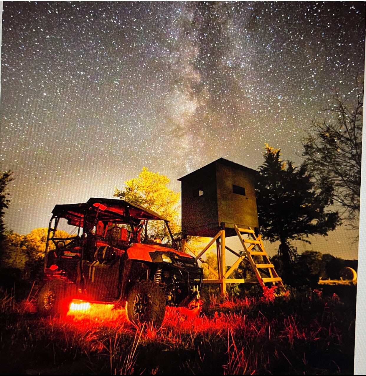 A tractor in a field with a starry sky above and a silo in the background.