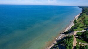Vista aérea de una zona costera con mar azul turquesa, una playa de arena y un paisaje verde con edificios.