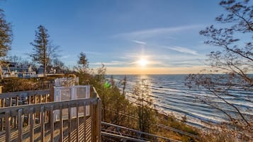A coastal view with a wooden deck overlooking the sea, a clear sky, and a sunset.