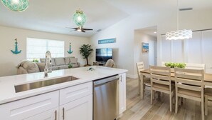 A modern kitchen with a central island, white cabinetry, and a dining area with wooden chairs and a table.
