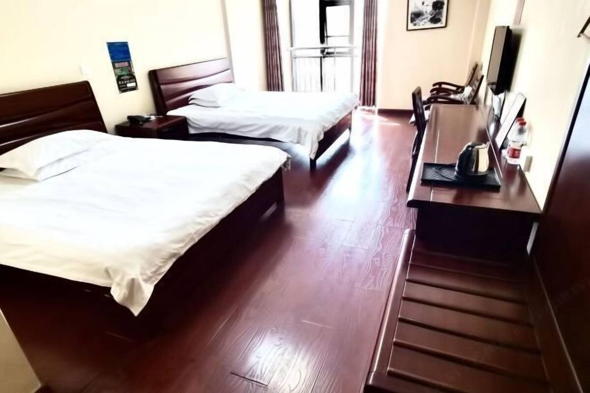 A hotel room with two beds, a wooden desk, a chair, a TV, and a window with curtains.
