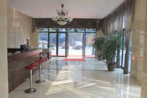 Un hall de hotel con mostrador de recepción, zona de estar y una planta grande en maceta.