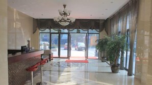 A hotel lobby with a reception desk, red bar stools, a chandelier, large windows, and potted plants. - Puyuan Qihonglou Hotel (Tongxiang)