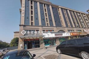 Un edificio de varios pisos con una entrada destacada, varias tiendas y un coche estacionado.