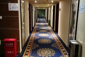 Un pasillo de hotel con alfombra estampada, un extintor y un cubo de basura.