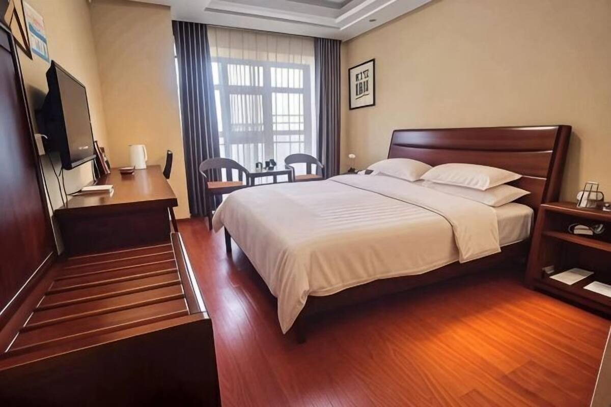A hotel room with a bed, a desk, a chair, a TV, and a window with curtains.