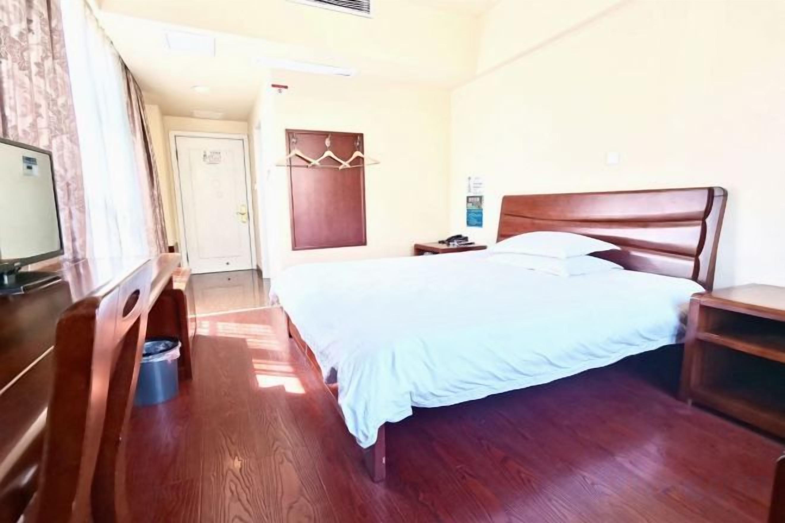 A hotel room with a bed, a desk, a chair, a television, and a wardrobe.