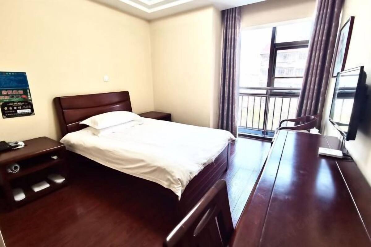 A hotel room with a bed, a desk, a chair, a TV, and a window with curtains.
