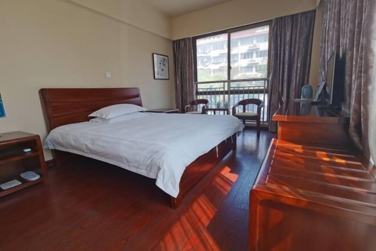 A hotel room with a large bed, a desk, a chair, and a view of buildings through the window.
