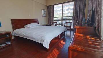 A hotel room with a large bed, a desk, a chair, and a view of buildings through the window.