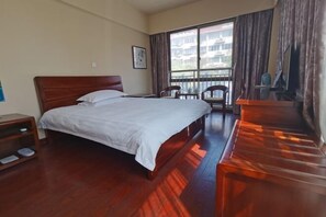 Habitación de hotel con una cama grande, un escritorio, una silla y vistas a edificios a través del ventanal.