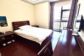 Habitación de hotel con cama, mesita de noche, escritorio, silla y ventana con cortinas.