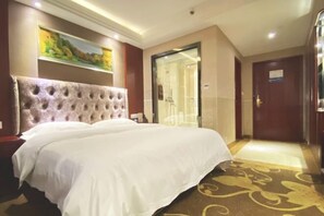 Una habitación de hotel con una cama grande, un cuadro en la pared y una puerta con un panel de cristal.