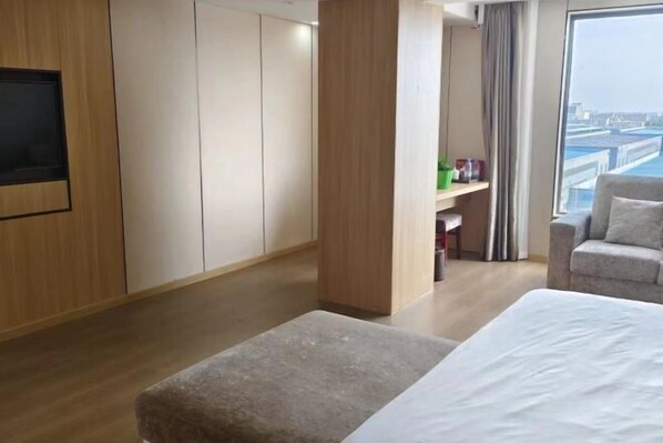 Habitación de hotel con cama, zona de estar, televisor y vistas a la ciudad.