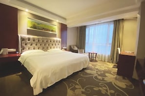 A hotel room with a large bed, a chair, a small table, and a painting on the wall. - Chongzhou Lanfeng Hotel (Chongzhou)