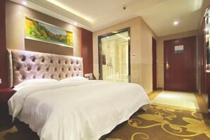 Habitación de hotel con una cama grande, un cuadro en la pared y una puerta que da a un pasillo.