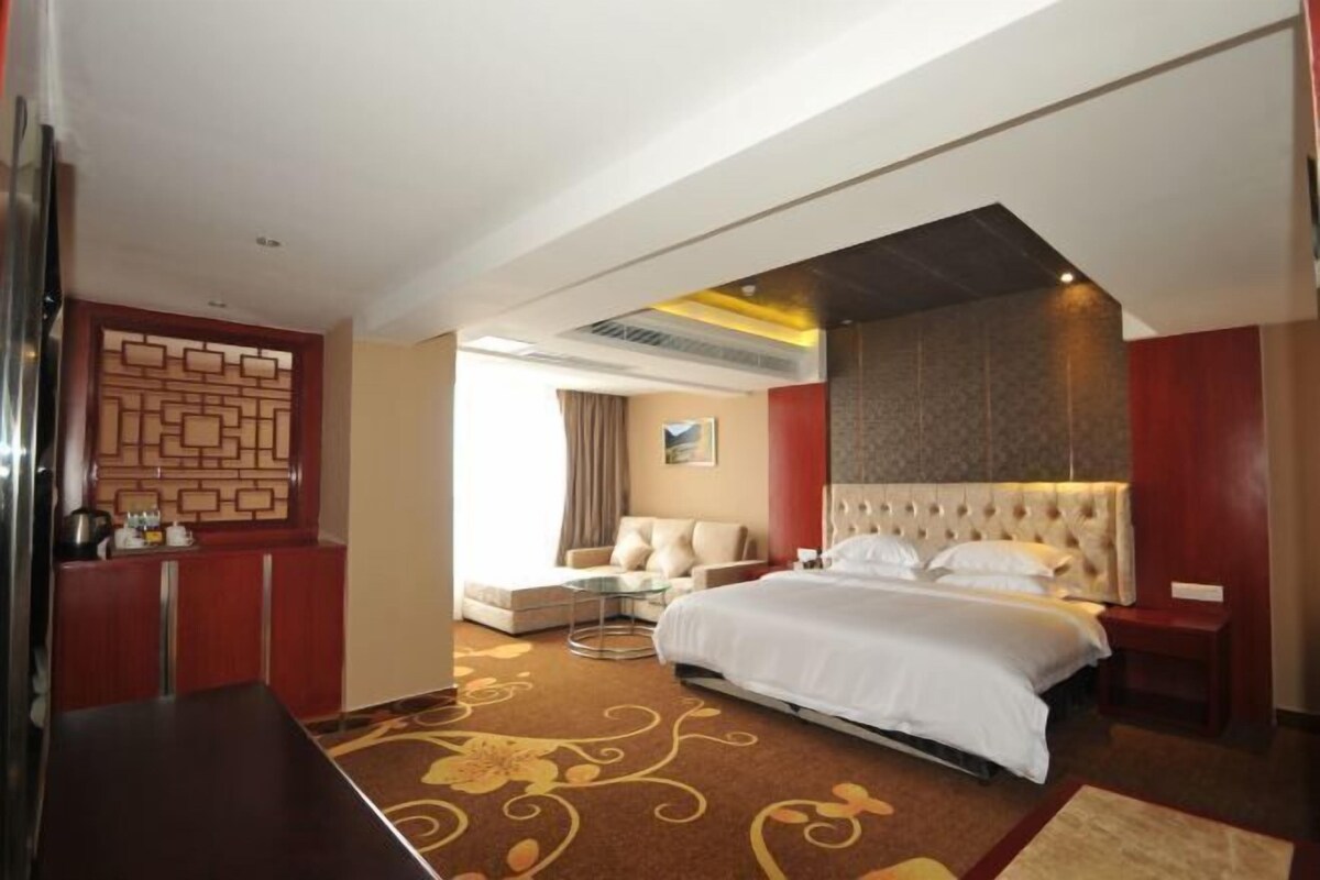 A hotel room with a bed, a sofa, a small table, and a decorative wall panel.
