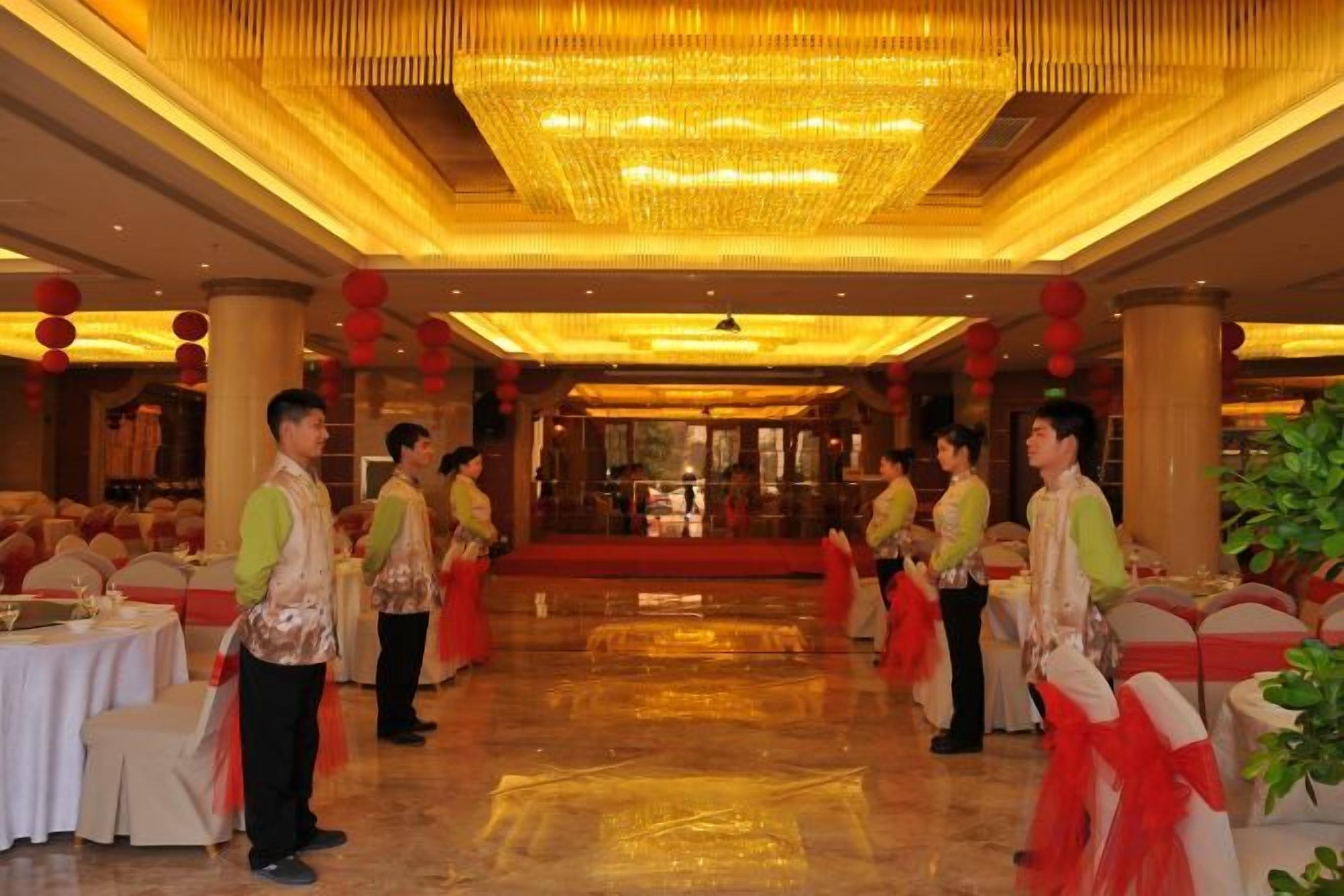 Un gran saló de banquets amb taules preparades per a un esdeveniment formal, una pèndol i decoracions vermelles.