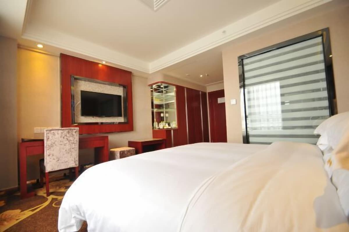 A hotel room with a large bed, a television, a mirror, and a wardrobe.