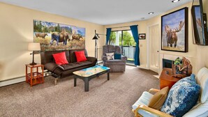 A living room with a brown leather sofa, a grey armchair, a coffee table, and a large painting of moose. - Sneaky Moose Townhome, 2BR / 2BA (Kenai)