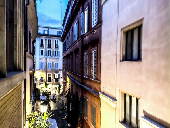 A narrow street with buildings on either side, a small outdoor seating area, and a visible entrance to a building.