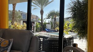 Ein modernes Wohnzimmer mit Ledersofa, Couchtisch und Blick auf einen Pool und Palmen draußen.