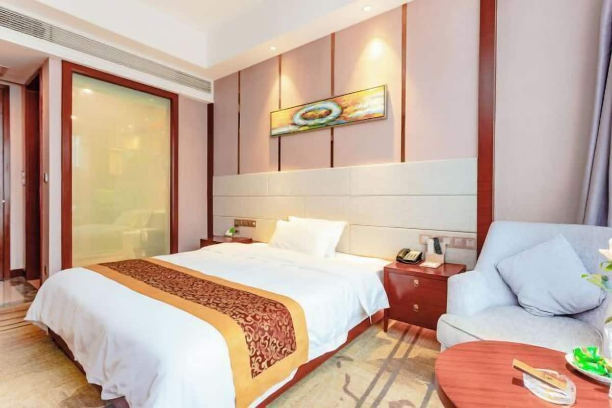 A hotel room with a large bed, a sofa, a small table, and a painting on the wall.