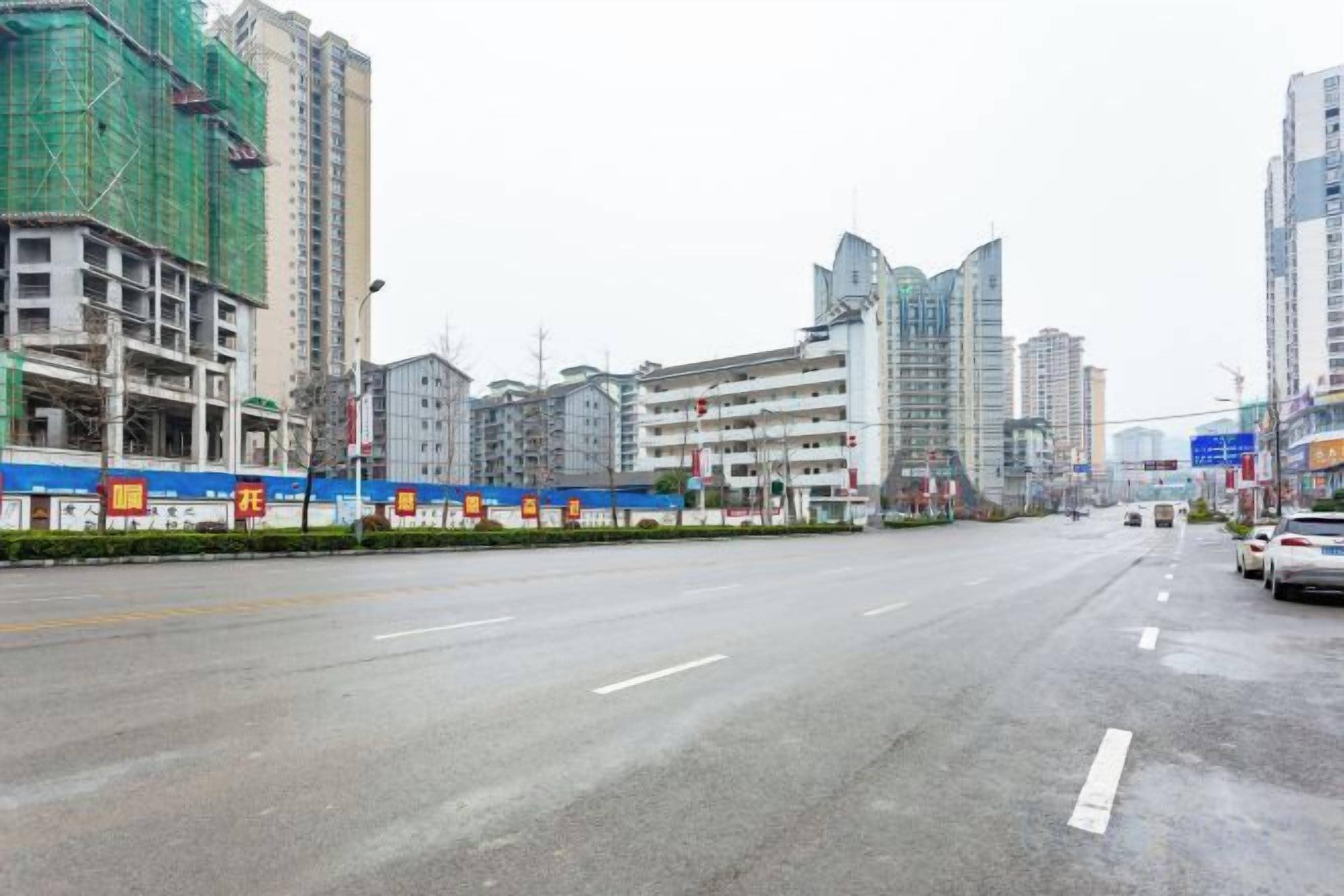 Una amplia avenida urbana con edificios de varios pisos, algunos en construcción, y un cielo despejado.
