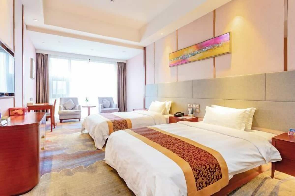 A hotel room with two beds, a desk, a chair, and a large window.