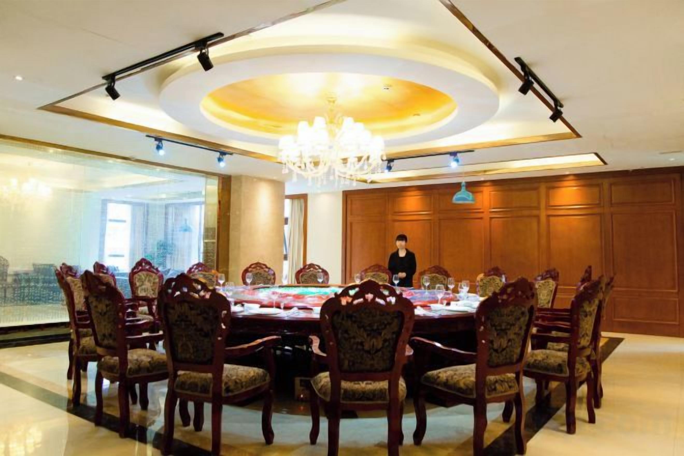 A conference room with a round table, chairs, a chandelier, and a person standing.