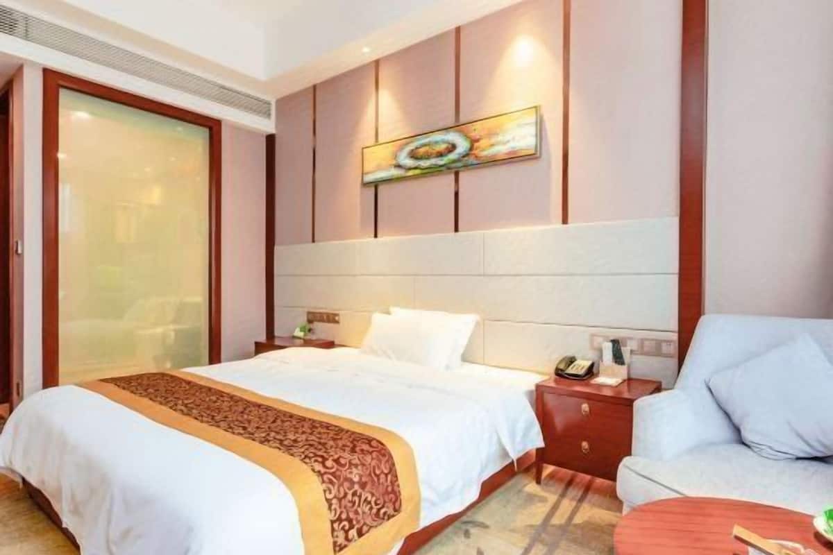 A hotel room with a bed, a sofa, a small table, and a painting on the wall.