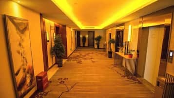 Un pasillo de hotel con piso alfombrado, plantas en macetas y obras de arte en las paredes.