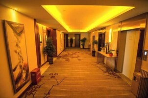 Un pasillo de hotel con piso alfombrado, plantas en macetas y obras de arte en las paredes.