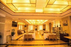 A hotel dining area with multiple tables and chairs, a central chandelier, and a television mounted on the wall. - Si Chen Hotel (Yinjiang)