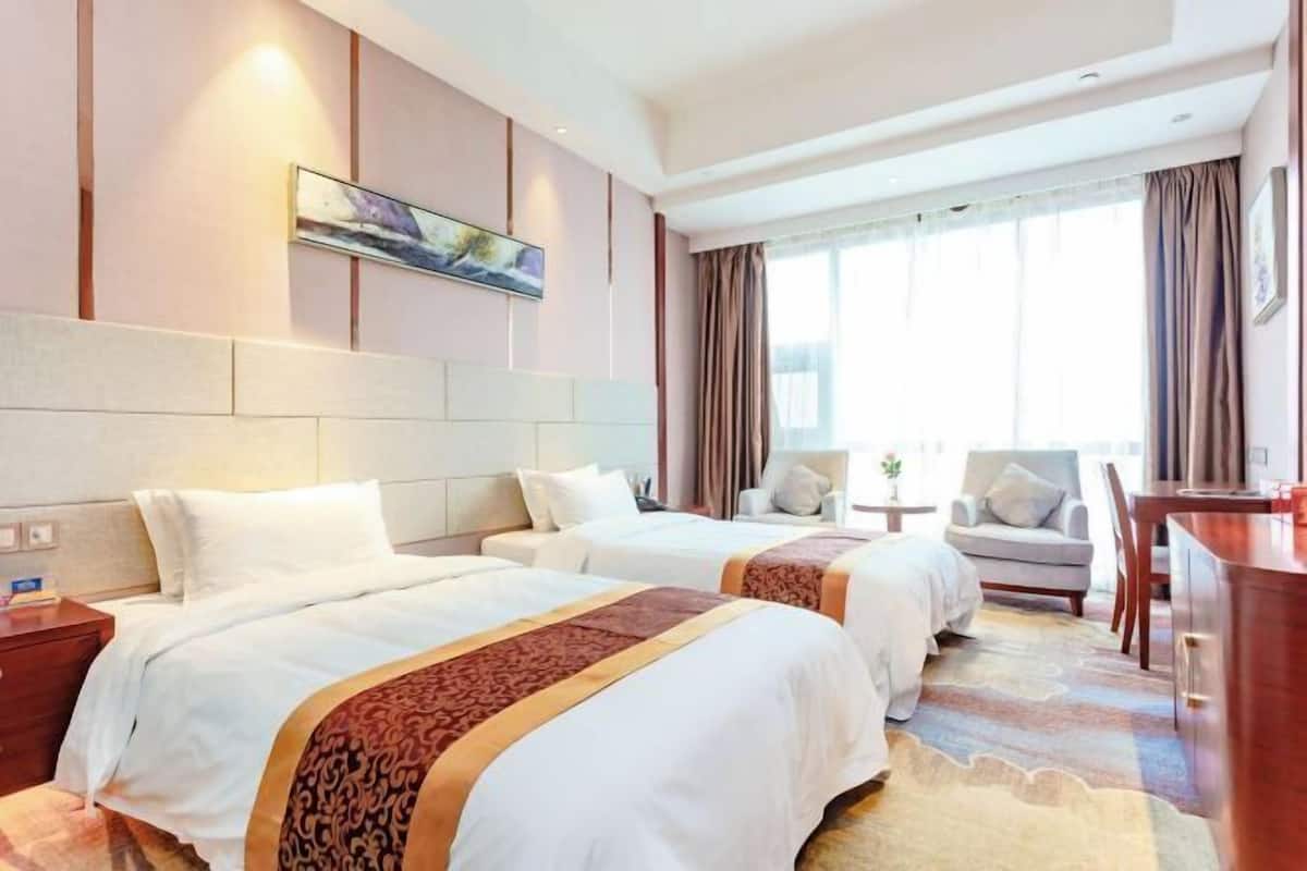 A hotel room with two beds, a desk, and a chair.
