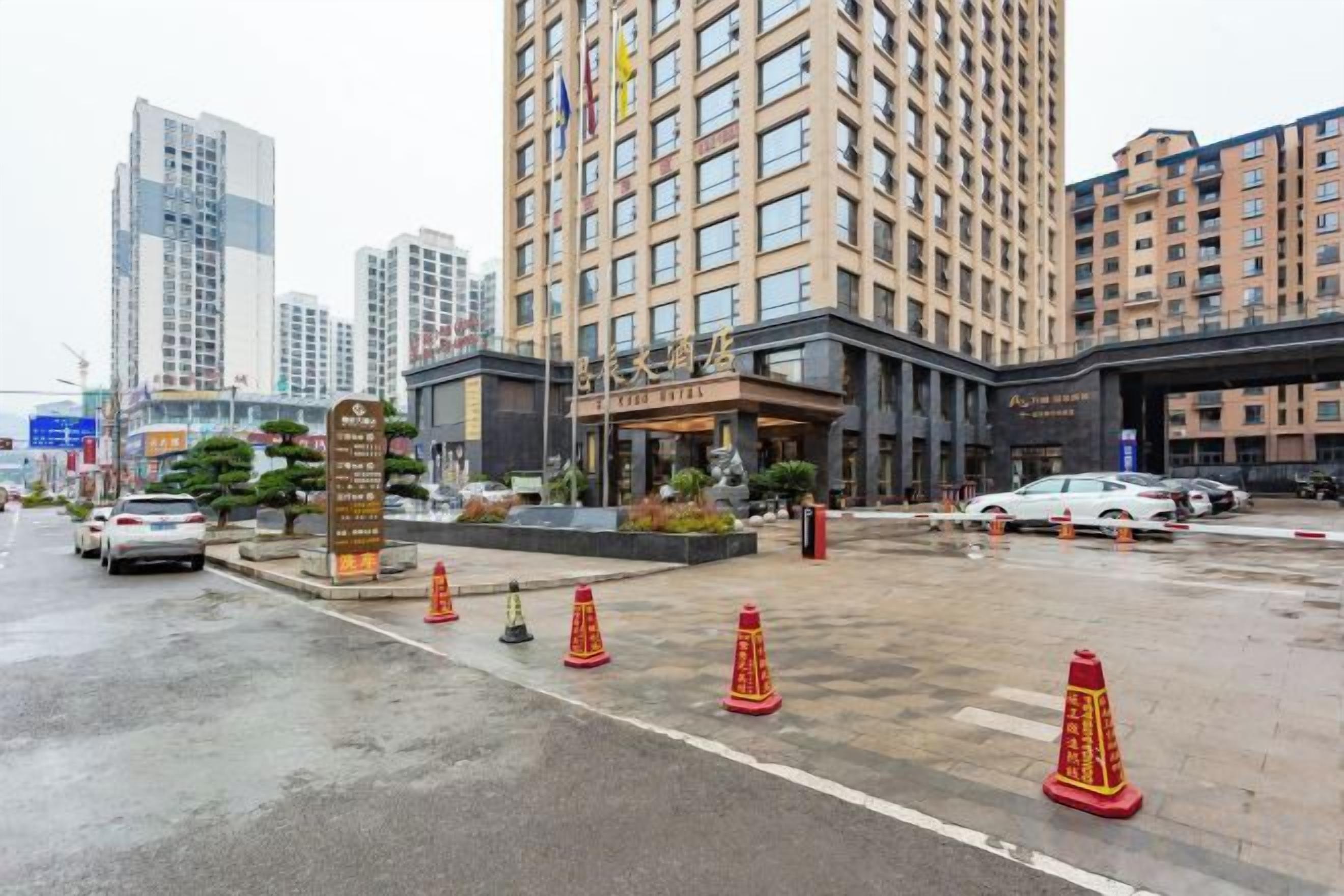 Entrada de un hotel con un edificio grande al fondo, pavimento mojado y conos de tráfico.