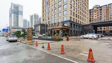 Entrada de un hotel con un edificio grande al fondo, pavimento mojado y conos de tráfico.