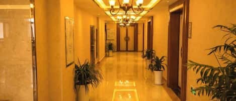 A hotel hallway with a polished floor, potted plants, and a chandelier.