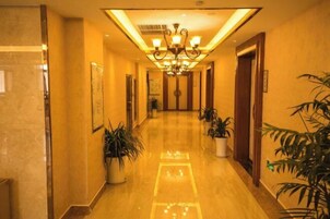 Un pasillo de hotel con piso pulido, plantas en macetas y un candelabro.