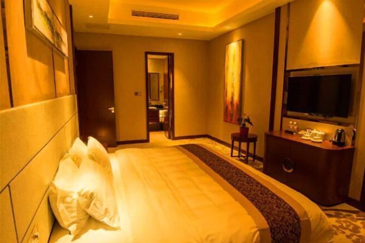 A hotel room with a large bed, a television, a desk with a telephone, and a mirror.