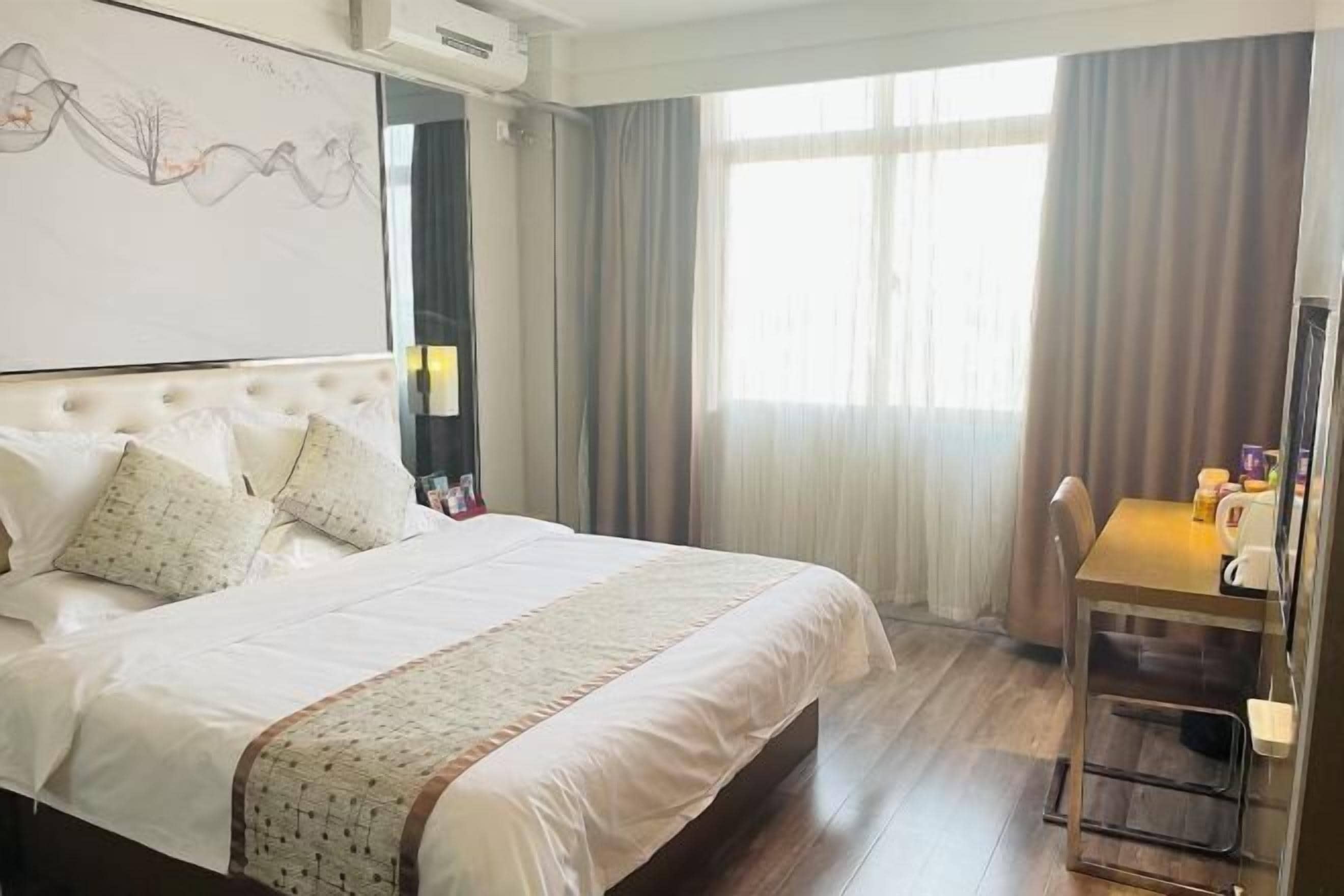 A hotel room with a large bed, a desk, and a window with curtains.