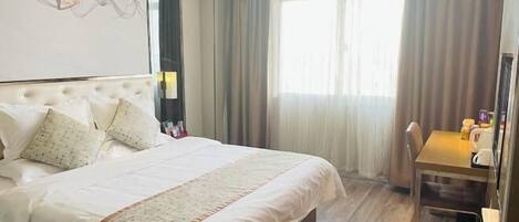 A hotel room with a large bed, a desk, and a window with curtains.