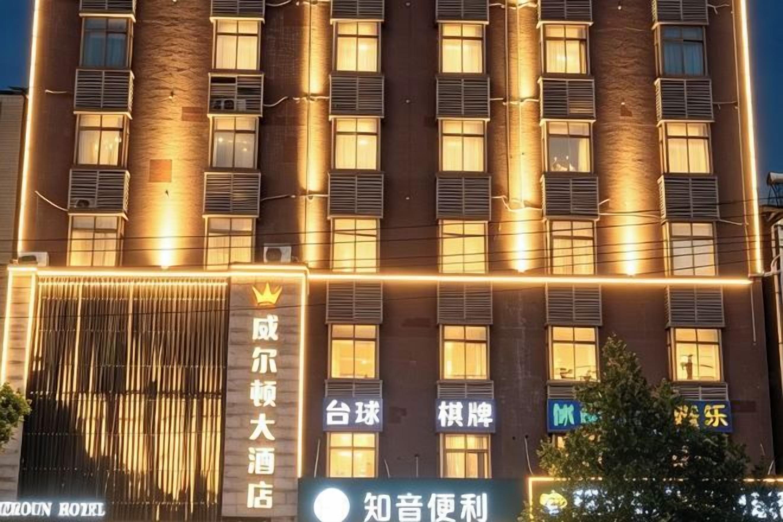 Un hotel de varios pisos, con ventanas iluminadas y un cartel llamativo con caracteres chinos.